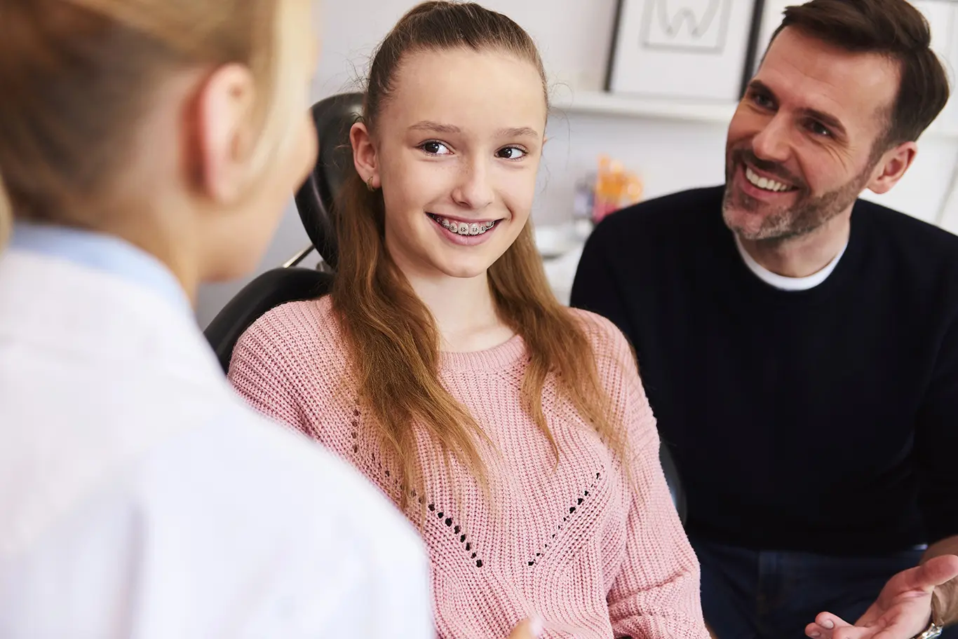 A teenager and her Dad listen to the orthodontist to learn more about the future treatments.